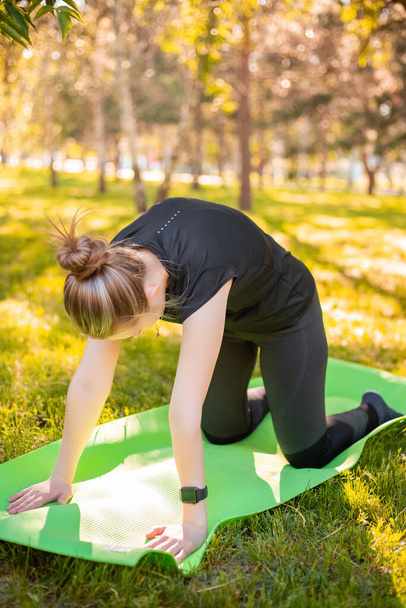 Outdoor fitness and pilates workout. A young woman does exercises to stretch the muscle,  while sitting on a yoga mat in the park. Exercise to develop flexibility.  - Foto, Imagen