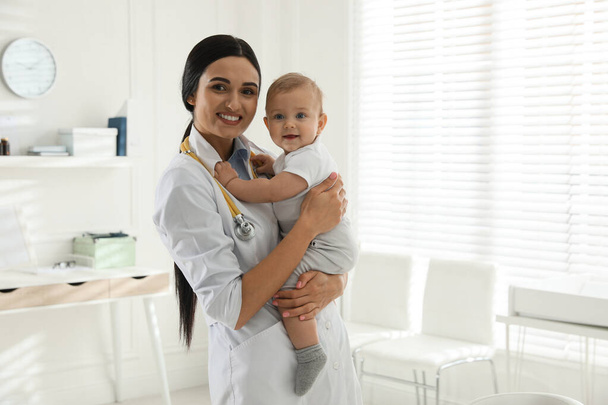 Young pediatrician with cute little baby in clinic. Space for text - Zdjęcie, obraz