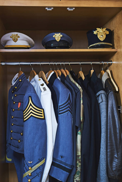 Ρούχα φτιαγμένα για μάχη. Πυροβολισμός διαφόρων στρατιωτικών σακάκια και καπέλα κρέμονται σε μια ντουλάπα. - Φωτογραφία, εικόνα