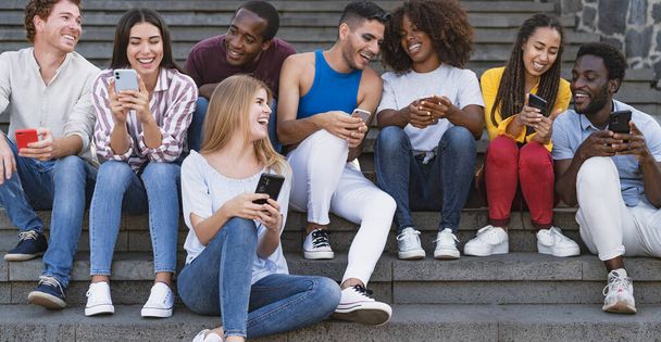 Junge multiethnische Freundesgruppe sitzt mit Handy auf der Treppe aus dem College - Millennial-Lifestyle-Konzept der Jugend - Foto, Bild