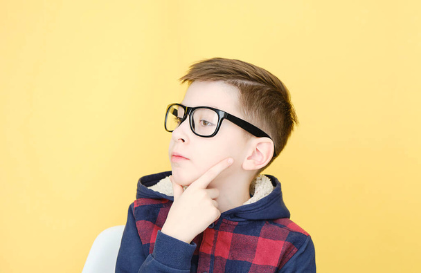 pensive boy with blonde hair and glasses isolated on yellow. - Foto, afbeelding