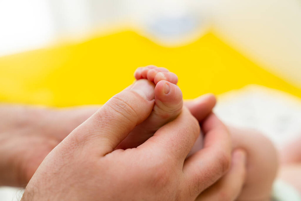Hands of mother holding baby newborn feet with love. Little lines and wrinkles on tender feet. Cute and tiny baby feet on parent hand at cozy home - Photo, Image