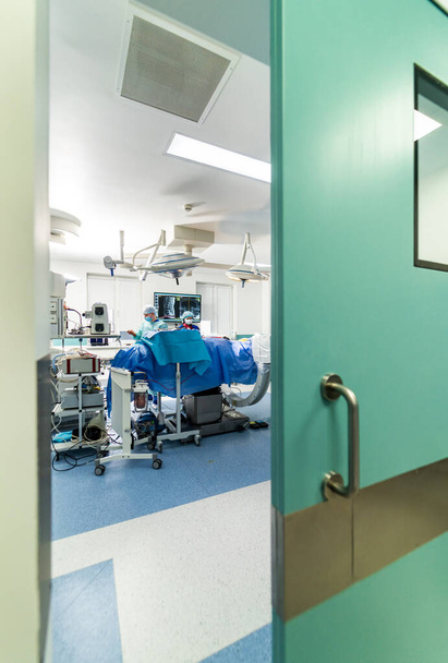 View from the door at the group of neurosurgeons in operating room with surgery equipment. Doctors using hi-tech equipment. Modern medical background. - Φωτογραφία, εικόνα