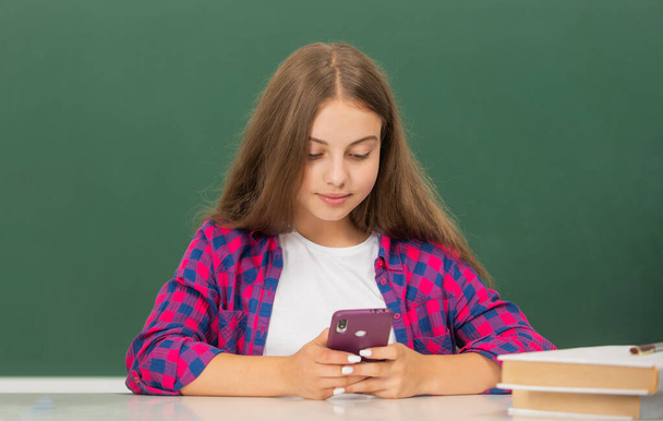 busy teen girl typing message on mobile phone in high school at blackboard, message - Photo, image