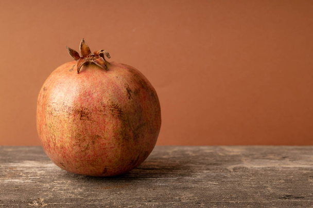 fruta de granada sobre un fondo similar en color a la piel. viejo soporte de madera de la fruta - Foto, Imagen