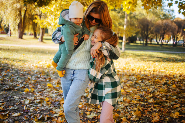 Junge Mutter spaziert mit Baby und großer Schwester im Herbstpark. - Foto, Bild