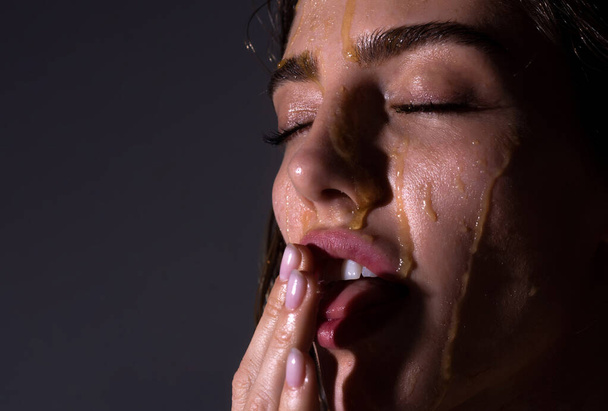 Fashion and beauty. Sensual young woman face with honey drop close up. Sexy model with honey drip on face. - 写真・画像