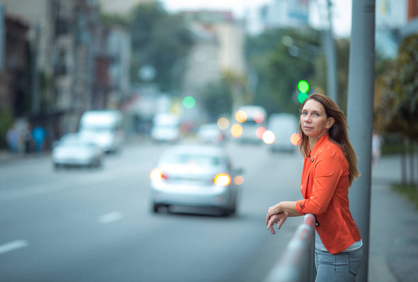 Retrato de una mujer hermosa y exitosa en una calle de la ciudad. La mujer está vestida con pantalones vaqueros y una chaqueta roja.. - Foto, imagen