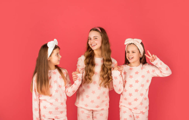 Homewear and pyjamas for children. Happy sisters in homewear. Holding hands and giving V sing - Foto, immagini