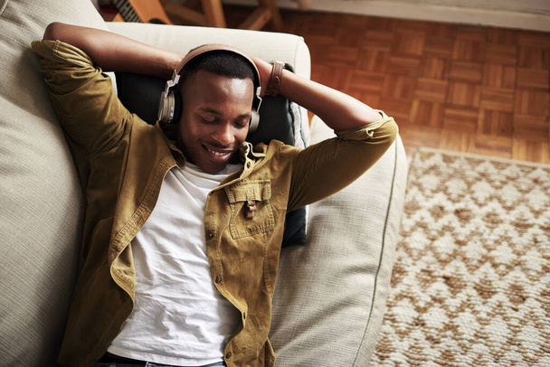 This is a really good song. High angle shot of a handsome young man smiling with his eyes closed while listening to music on his headphones at home. - Foto, Imagen