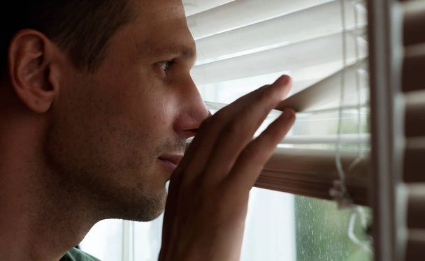 Young man peeking through blinds at home during quarantine.  - Fotoğraf, Görsel