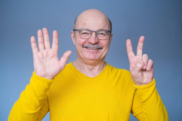 Hombre mayor levantando la mano, mostrando el número siete con los dedos, contando algo - Foto, imagen