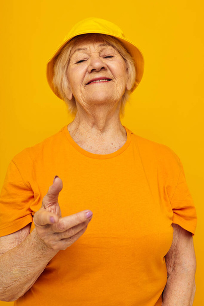 χαμογελαστή ηλικιωμένη γυναίκα με κίτρινα μπλουζάκια καπέλο με απομονωμένο φόντο - Φωτογραφία, εικόνα