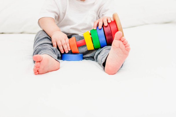 Close-up kind van 1 jaar oud met wit tshirt spelend met houten piramide. Concept van houten speelgoed, ontwikkeling van kinderen - Foto, afbeelding