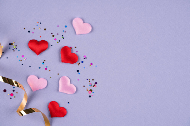 Valentine's day festive background. Pink and red hearts with multicolored confetti around on purple background with copy space. Flat lay, top view. Greeting card, invitation - Photo, Image