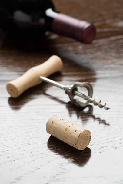 Abstrakcyjna butelka wina, korkociąg i korkociąg układające się na refleksyjnej powierzchni drewna. - Zdjęcie, obraz