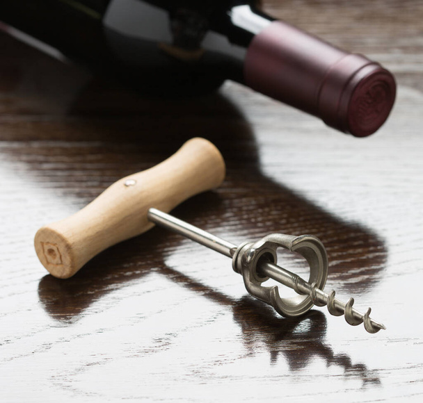 Garrafa de vinho abstrata e saca-rolhas deitadas em uma superfície de madeira reflexiva. - Foto, Imagem