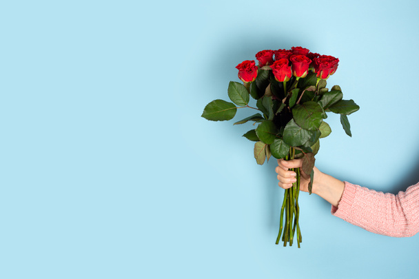 Ruka drží Krásné velké kytice červené růže světle modré pozadí. Módní plakát na Valentýna, Mezinárodní den žen nebo Den matek. Nápis s mezerou pro kopírování - Fotografie, Obrázek
