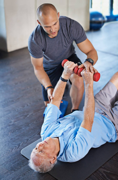 Guiding him back to wellness. Shot of a physiotherapist helping a senior man with weights. - Photo, image