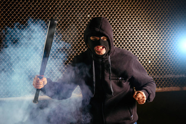 Masked angry man with bat in smoke. - Фото, изображение