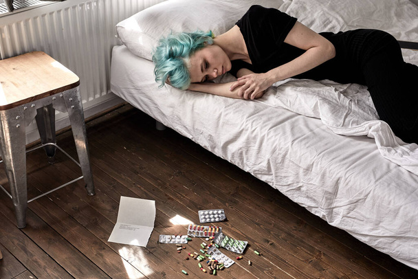 pills spread on floor, female lying on bed after taking pills overdose, at home - Фото, изображение
