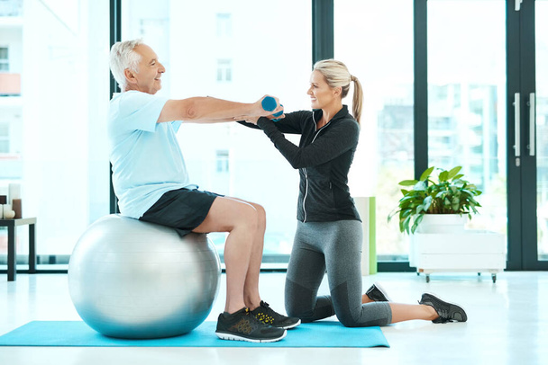 Working on all those stiff muscles. Shot of a physiotherapists helping her senior patient with his exercises in a fitness center. - Photo, image