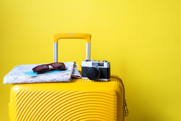 yellow suitcase, photo camera, glasses and map - traveler's accessories on a yellow background. travel concept - Photo, image