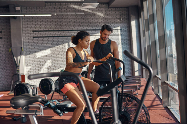 Male trainer look at orbitrek while girl exercise - Fotó, kép