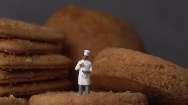 Çıtır bir kurabiyenin üzerinde duran minyatür bir şef. Minyatür insanlar ve iş konsepti. - Video, Çekim