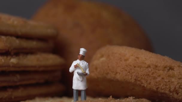 Két miniatűr séf áll egy ropogós sütin. Miniatűr emberek és üzleti koncepció. - Felvétel, videó