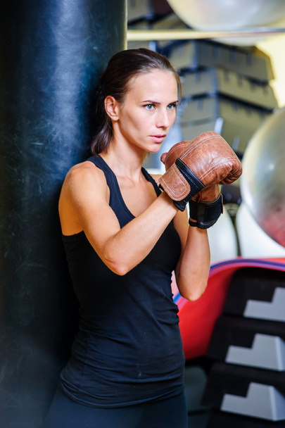 Beautiful sporty woman boxing with black punching bag at gym. - 写真・画像