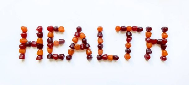Um grupo de gomas multivitamínicas vermelhas, laranja e roxas dispostas na forma da palavra saúde - Foto, Imagem