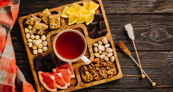 Menazhnitsa puupohjalla. Herkullista teetä, pähkinöitä ja suklaata puisella neliölautasella. Laadukas kuva - Valokuva, kuva