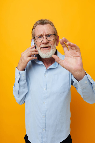 Portrait of happy senior man in a blue shirt and glasses talking on the phone cropped view - Fotó, kép