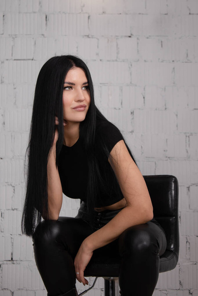 sexy brunette woman in black against white brick wall background. female fashion portrait - Foto, imagen