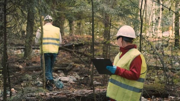 Uomo ecologista in abbigliamento da lavoro e casco pulito spazzatura plastica nella foresta - Foto, immagini