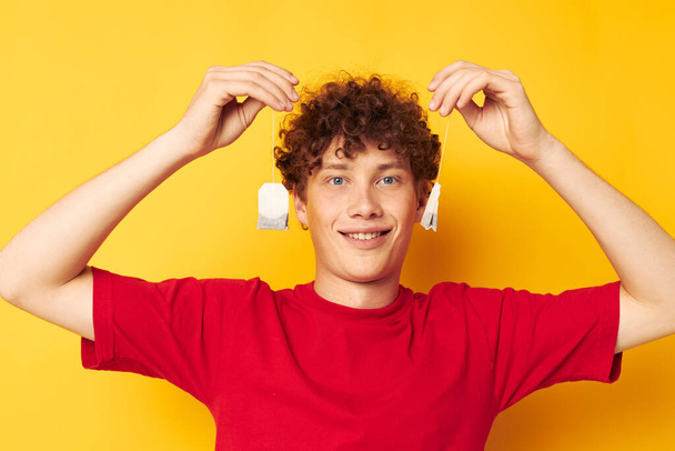Young curly-haired man posing tea disposable bags yellow background unaltered - Fotografie, Obrázek