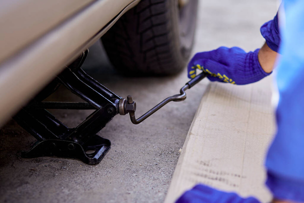 Lifting the auto with a jack-screw for tire changing. Lifestyle photography.  - Photo, Image