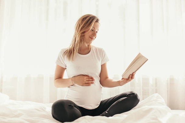 Pregnant woman reading book at home - 写真・画像