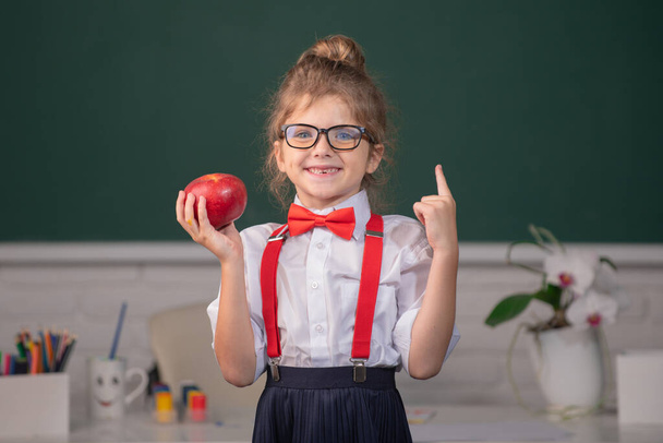Back to school. Portrait of school girl nerd student hold apple with surprising expression pointing with finger against blackboard. - Valokuva, kuva