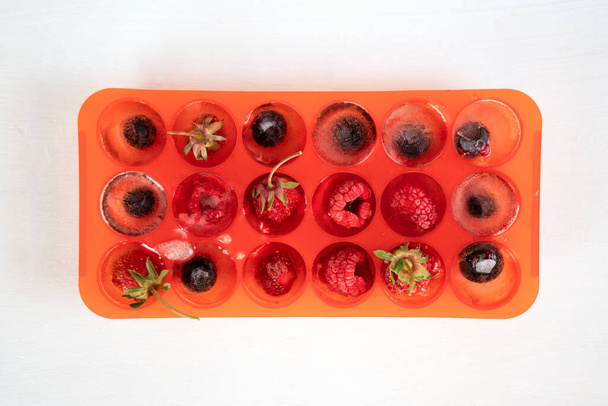 Frozen berries in ice cubes in red silicone tray or mold. Top view. - Foto, Bild