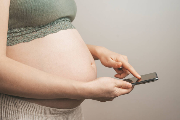 Mujer embarazada sosteniendo un teléfono con una pantalla en blanco, maqueta. Aplicaciones de embarazo, gadgets, movimiento y seguimiento de empuje, fondo de la dieta - Foto, Imagen