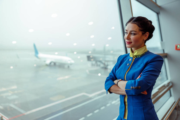 Kobieta stewardessa patrząc przez okno w terminalu lotniska - Zdjęcie, obraz