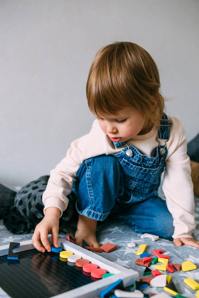 Ребёнок играет дома в образовательную игру с разноцветной магнитной головоломкой - Фото, изображение