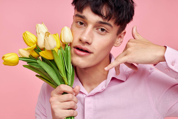 handsome guy in a pink shirt with a bouquet of flowers gesturing with his hands isolated background unaltered - Foto, Imagen