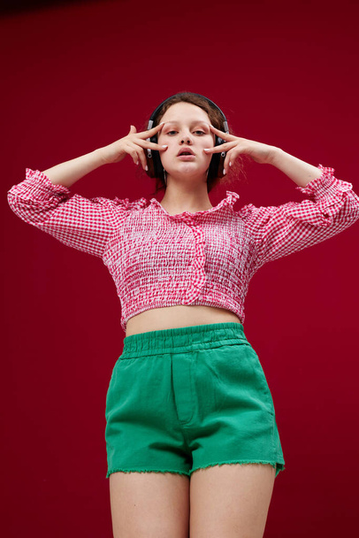 energetic young girl in green shorts listening to music Red background unaltered - Fotó, kép