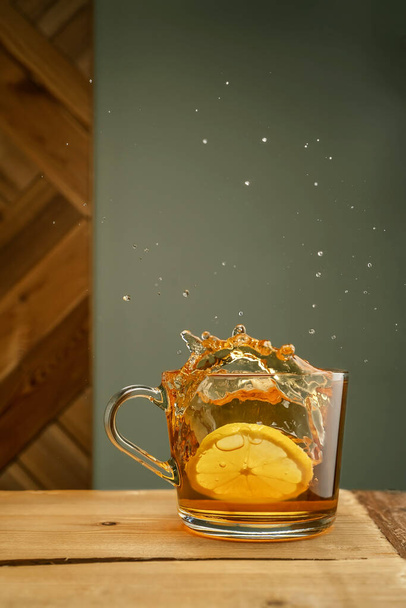Transparent mug with tea and splashes on a green background. - Zdjęcie, obraz