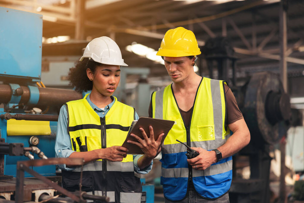 Portret pracownika produkcyjnego w dyskusji z inżynierem przemysłowym trzymającym tablet w fabryce. Biały brygadzista nadzoruje maszynę CNC. - Zdjęcie, obraz