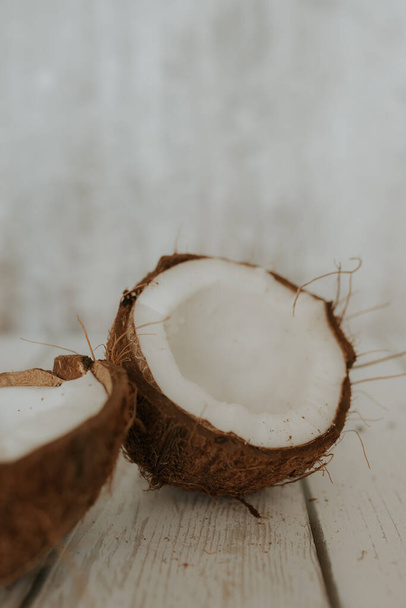 Coconut fruit on a wooden white floor. Two halves of a coconut lie on a light background. Selectiv focus. vertical photo - Foto, afbeelding