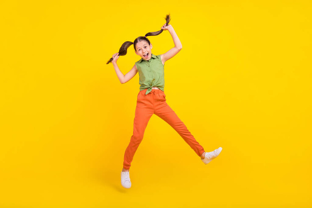 Photo of charming excited preteen girl dressed green top jumping high smiling isolated yellow color background - Zdjęcie, obraz